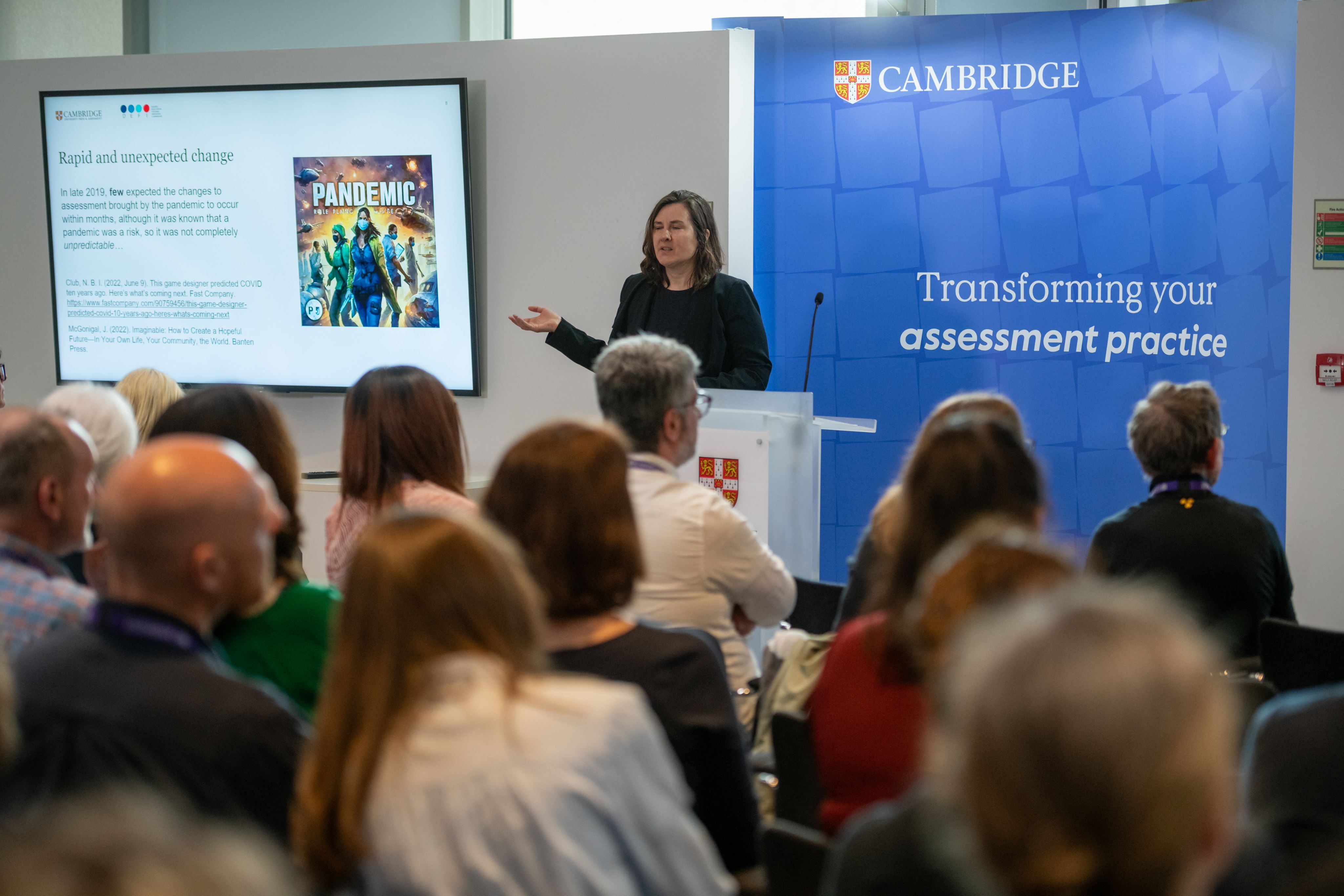 a speaker at Assessment Horizons conference standing on stage against blue Cambridge banner background