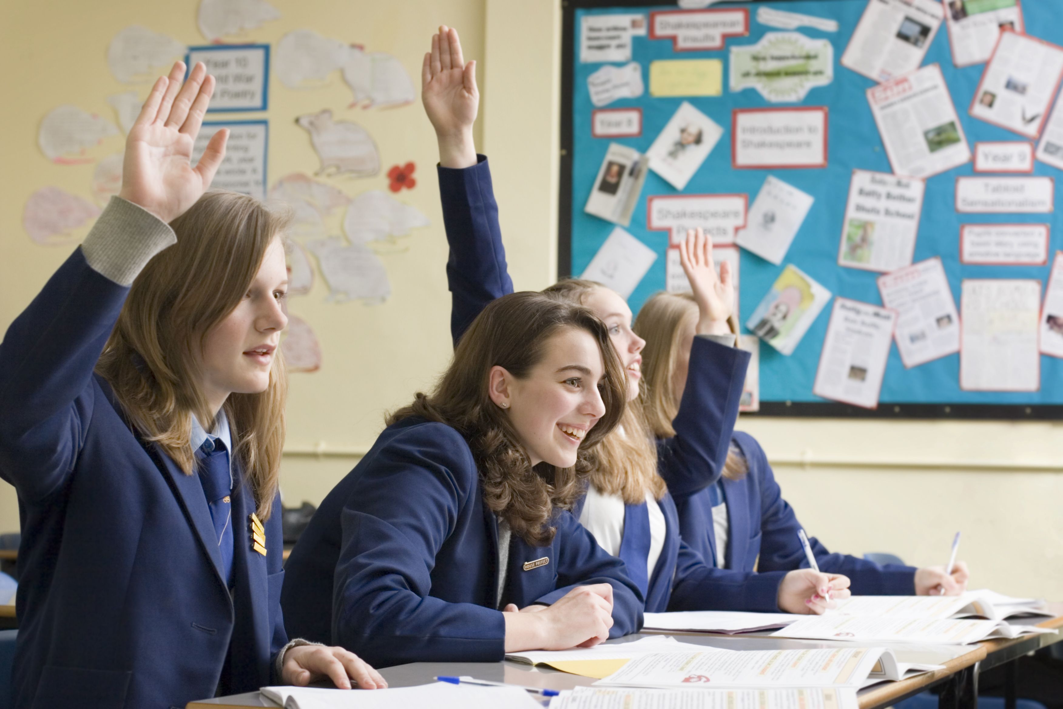 Students in uniform smile and put their hands up