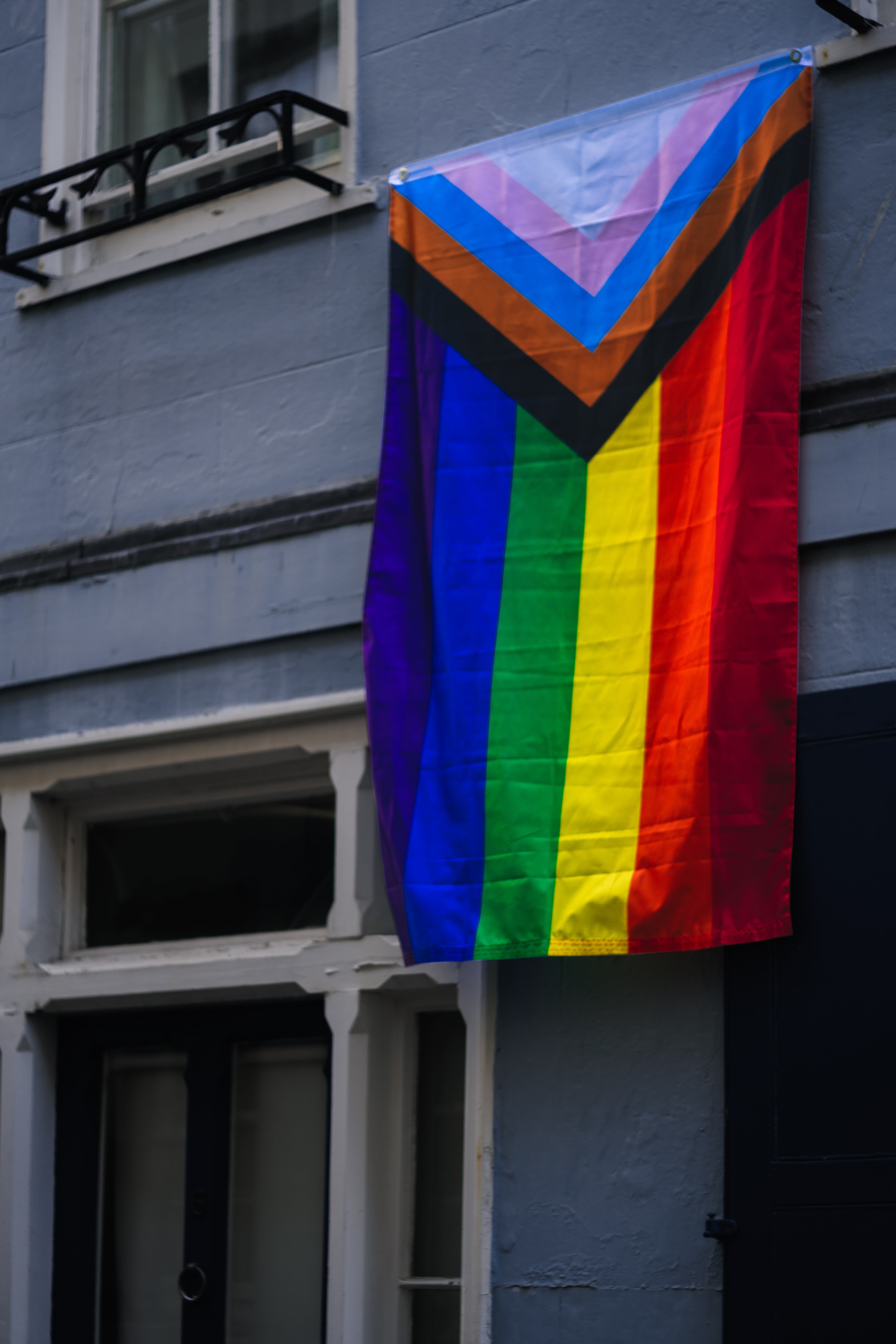 the rainbow coloured 'Progress Pride flag' hanging from the window of a grey building