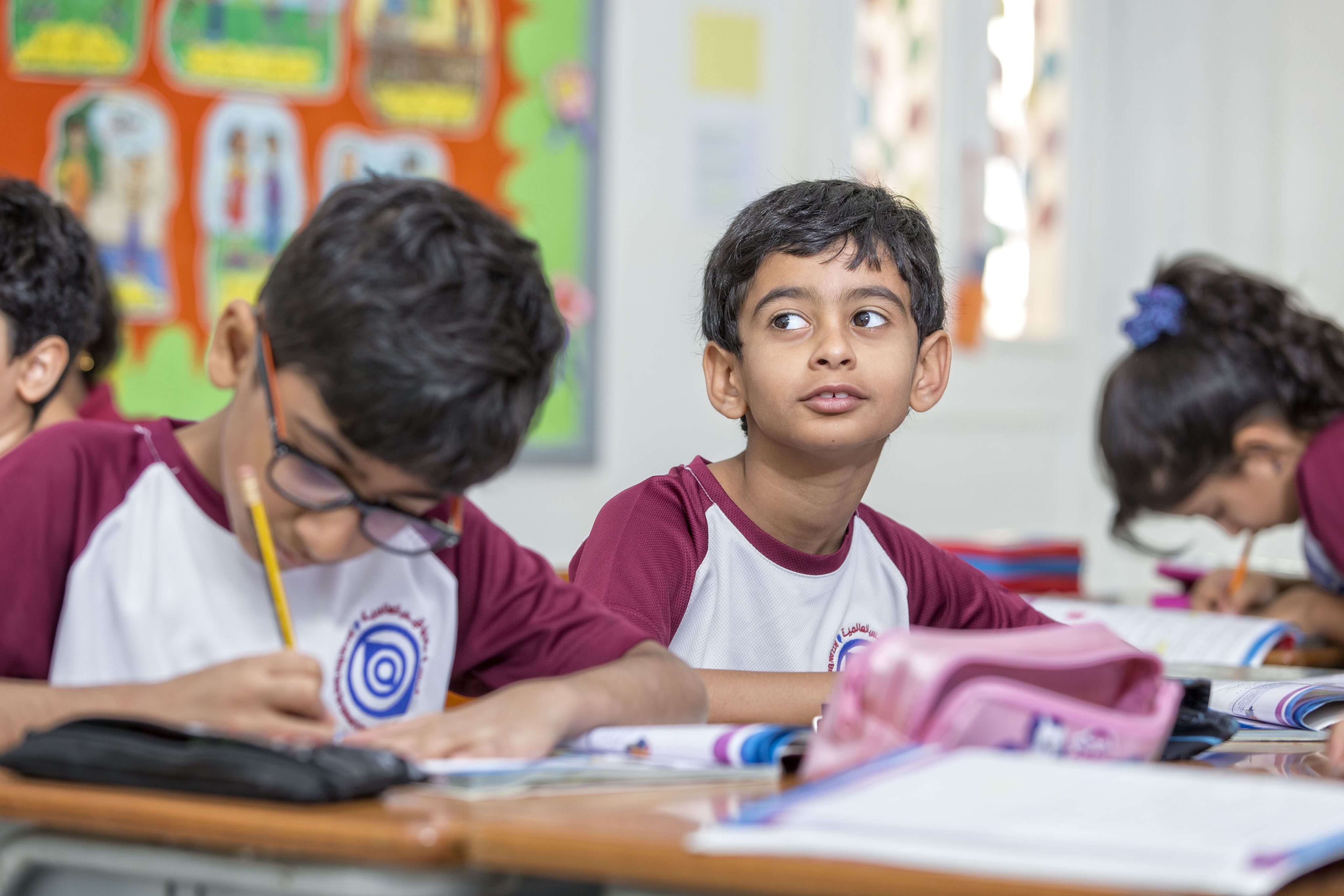 two young male learners wearing school uniforms working at their desks in class