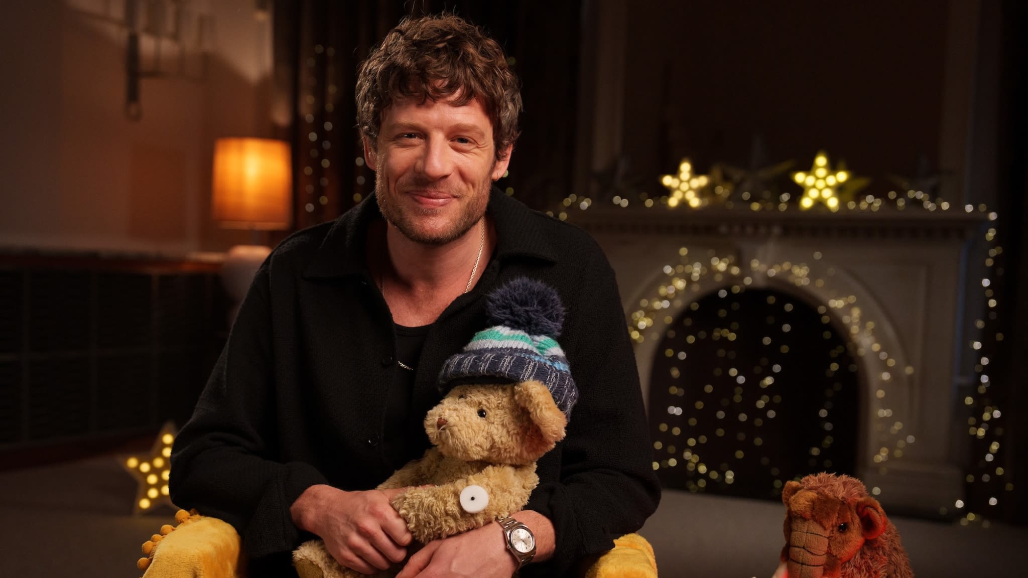 James Norton smiling to camera holding a teddy bear